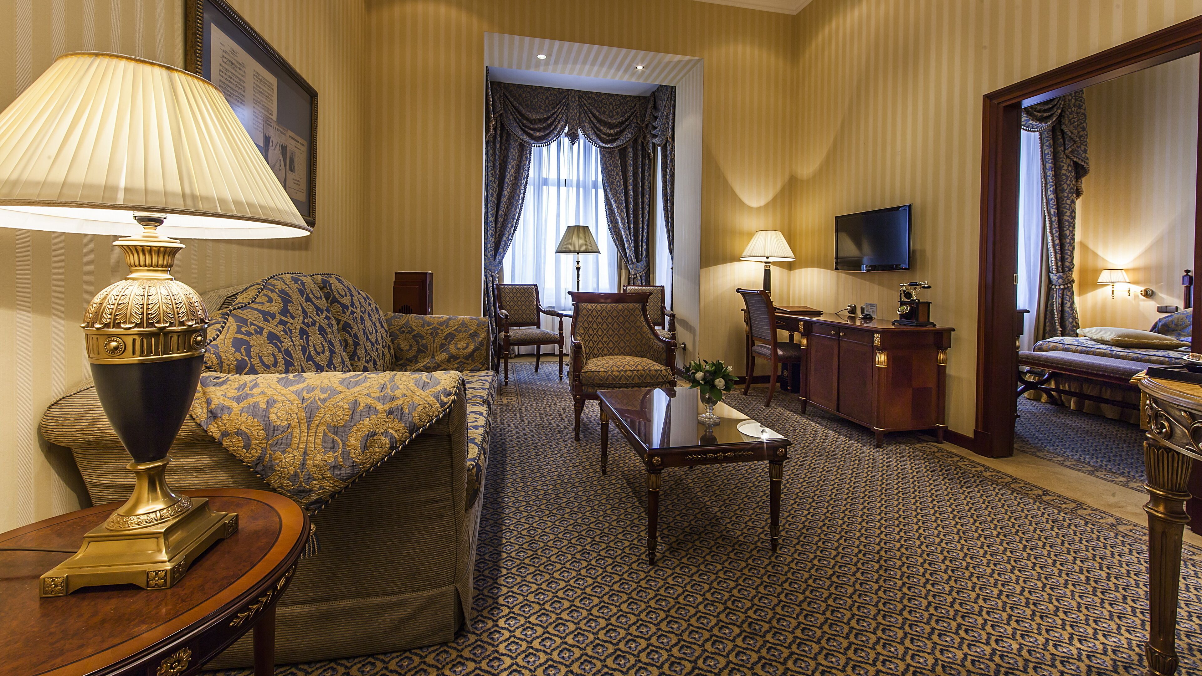A hotel room with a sofa, armchair, desk, and television.