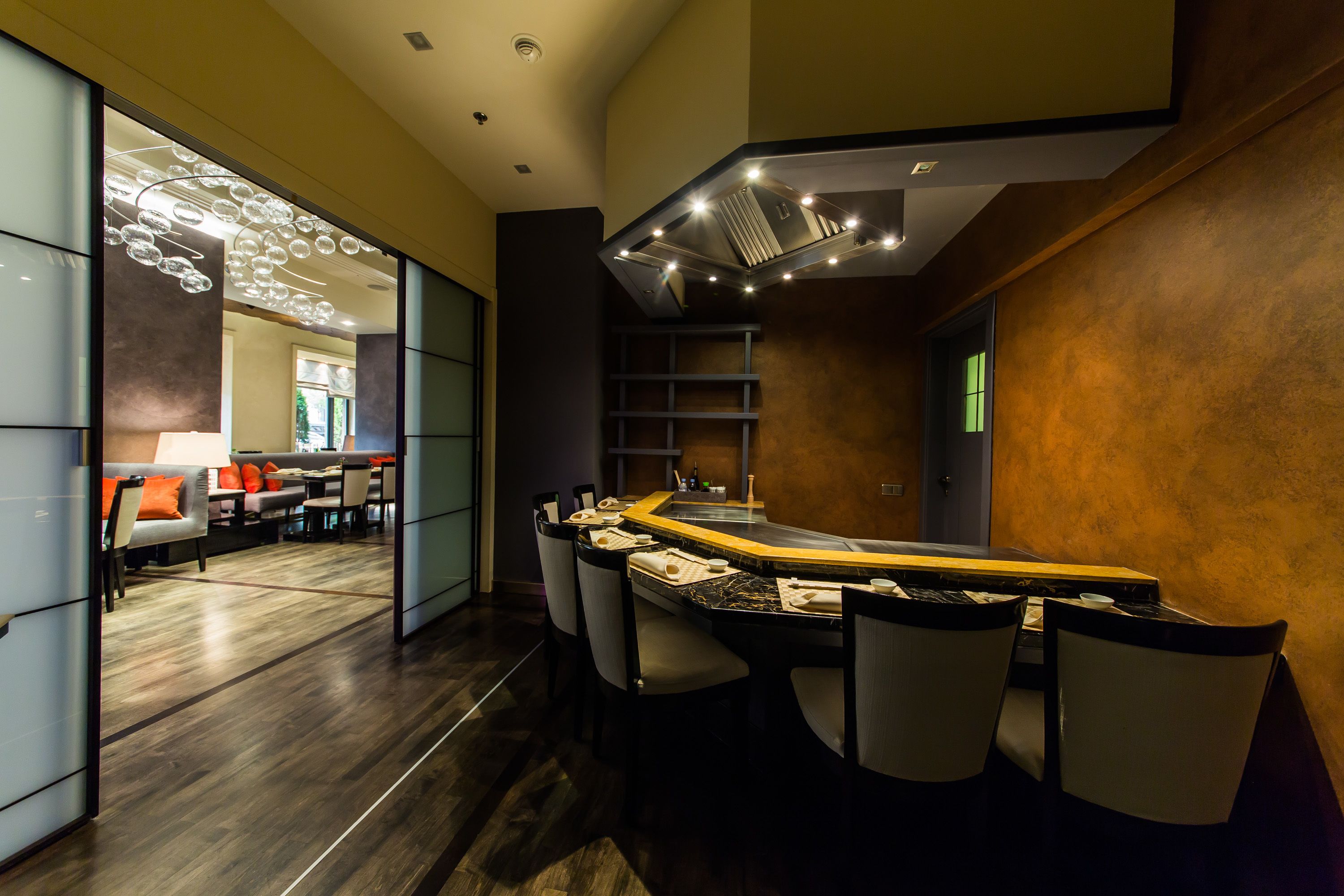 A modern dining area with a bar, seating, and a view of a lounge area.
