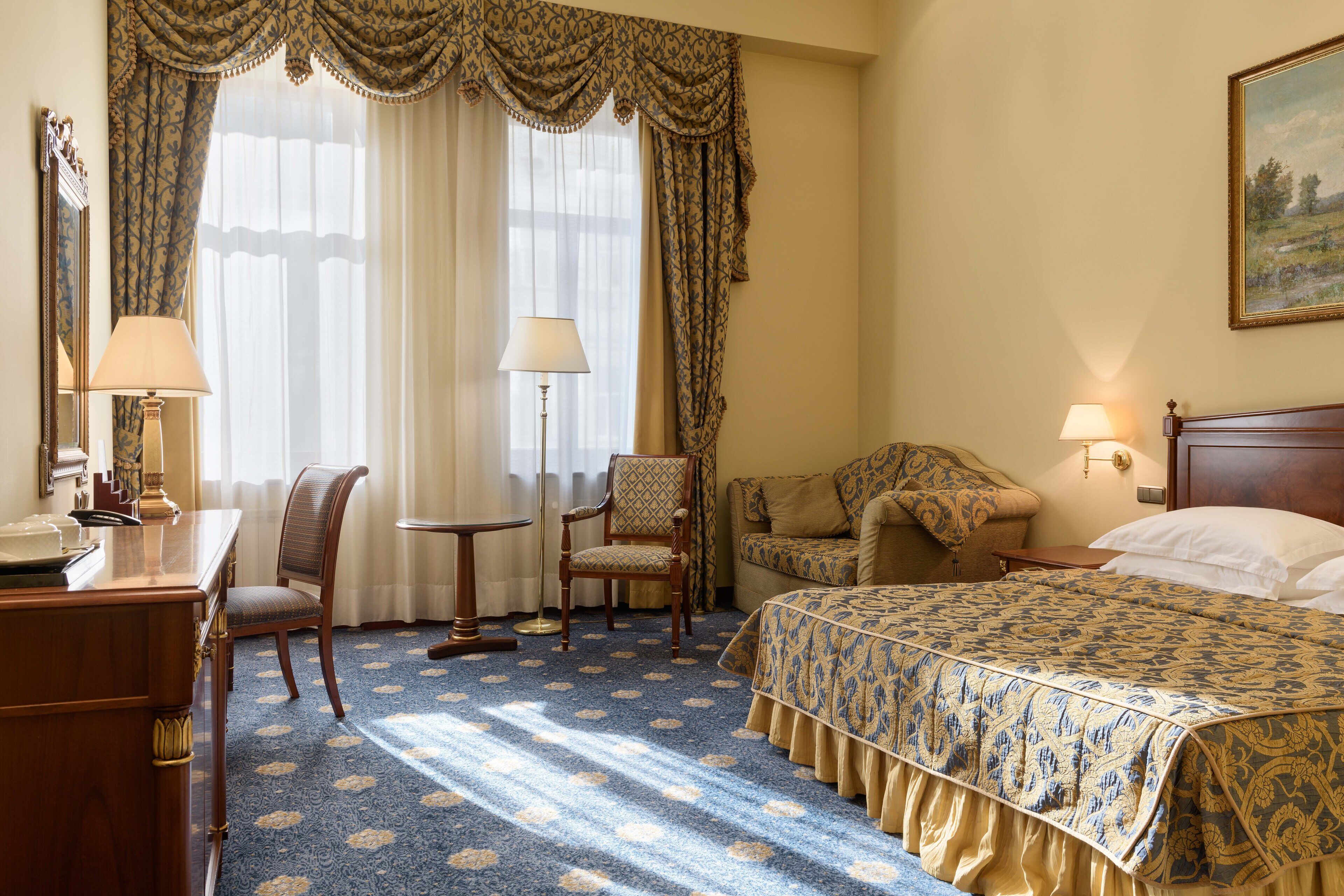 Habitación de hotel con cama, escritorio, silla, lámpara y un cuadro en la pared.