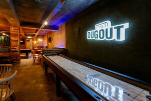 Una mesa de billar con un letrero de neón que dice "The Dugout" en una sala tenuemente iluminada con paredes y sillas de madera.
