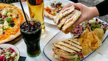 Een tafel met diverse etenswaren, zoals een belegd broodje, pizza, salade en friet.