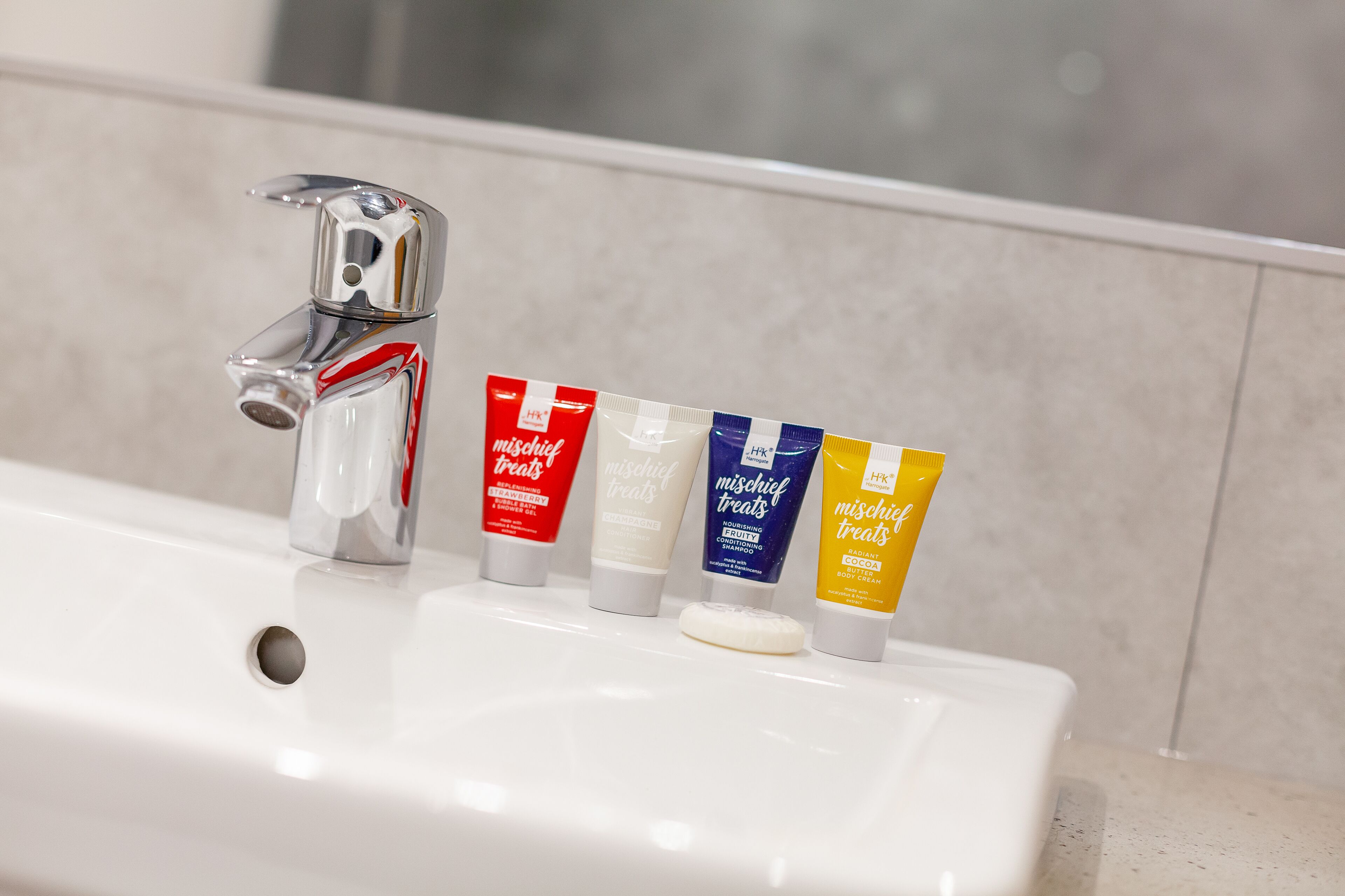 Uma pia de banheiro com quatro produtos de higiene: um vermelho, um branco, um azul e um amarelo, cada um com a etiqueta "mischief treats".