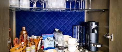 Una zona de bar con un salpicadero de azulejos azules, distintos vasos, botellas y una máquina de café.