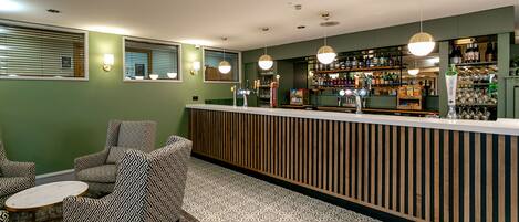 Una zona de bar con mostrador de madera, sillas estampadas y suelo de baldosas.