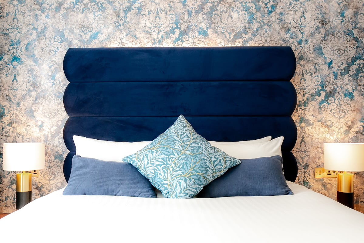 Una cama con cabecera oscura, dos lámparas de noche y almohadas estampadas.