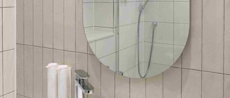 A bathroom with a large oval mirror, a white sink, and a shower area.