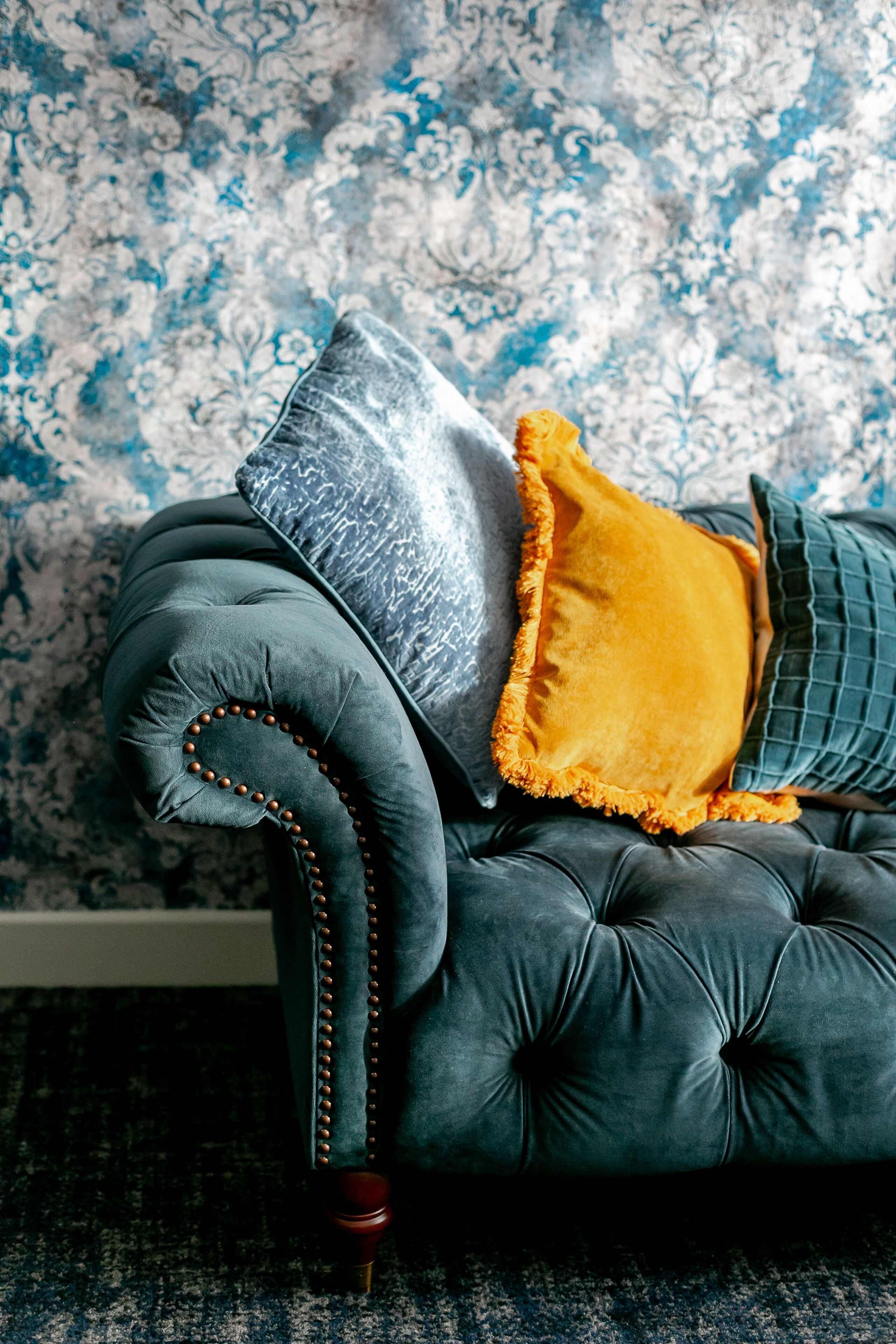 A tufted sofa with a dark fabric and wooden legs, accompanied by a grey and a yellow cushion.
