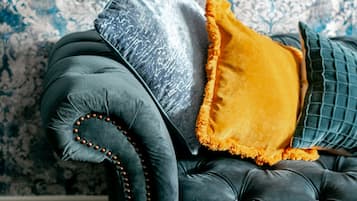 A tufted sofa with a dark fabric and wooden legs, accompanied by a grey and a yellow cushion.