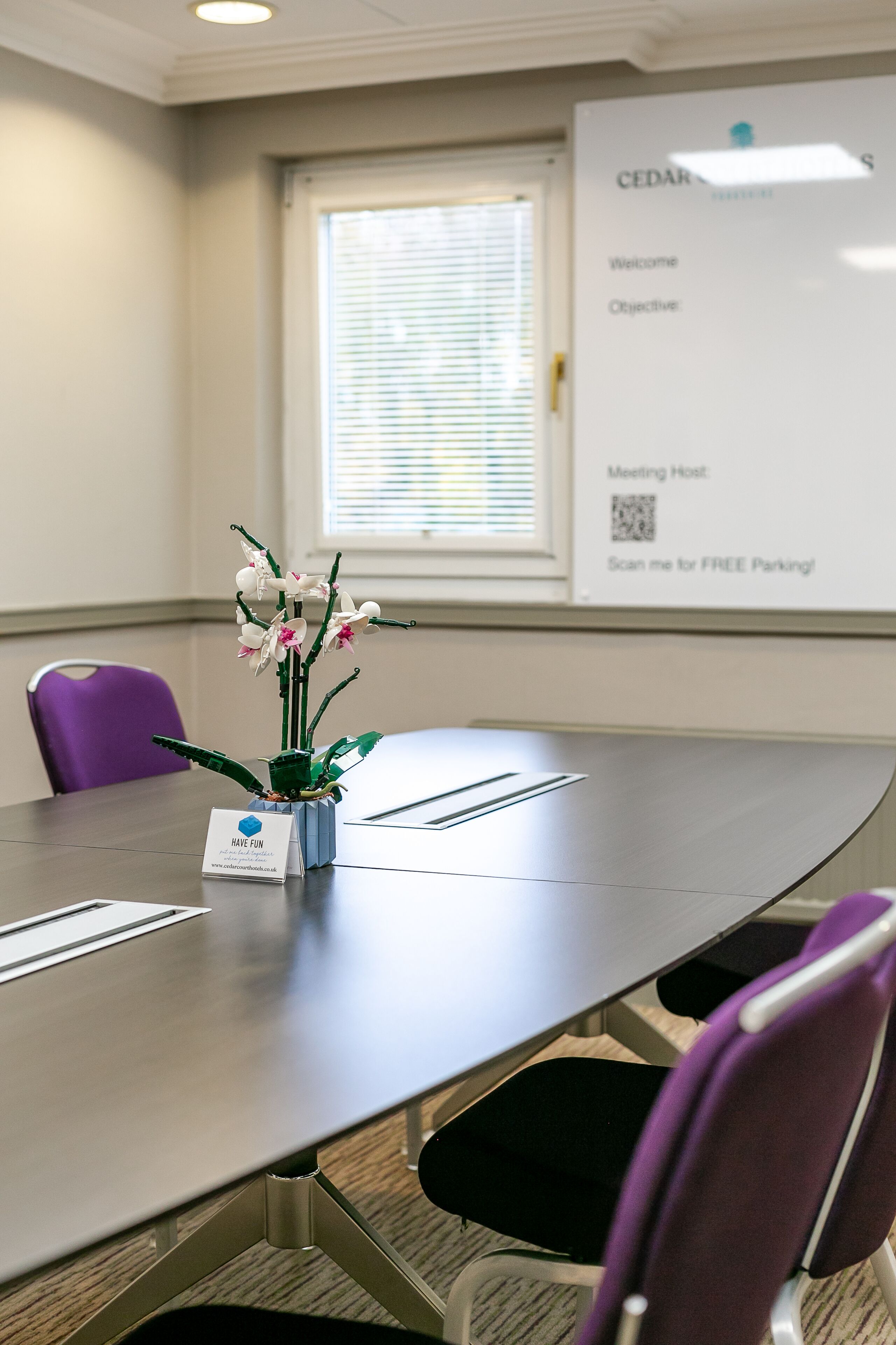 A conference room with a long table, purple chairs, a whiteboard, and a QR code for free parking.