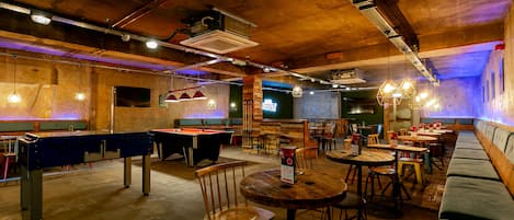 Une salle de billard équipée de tables et de chaises, de bancs en bois et de luminaires suspendus.