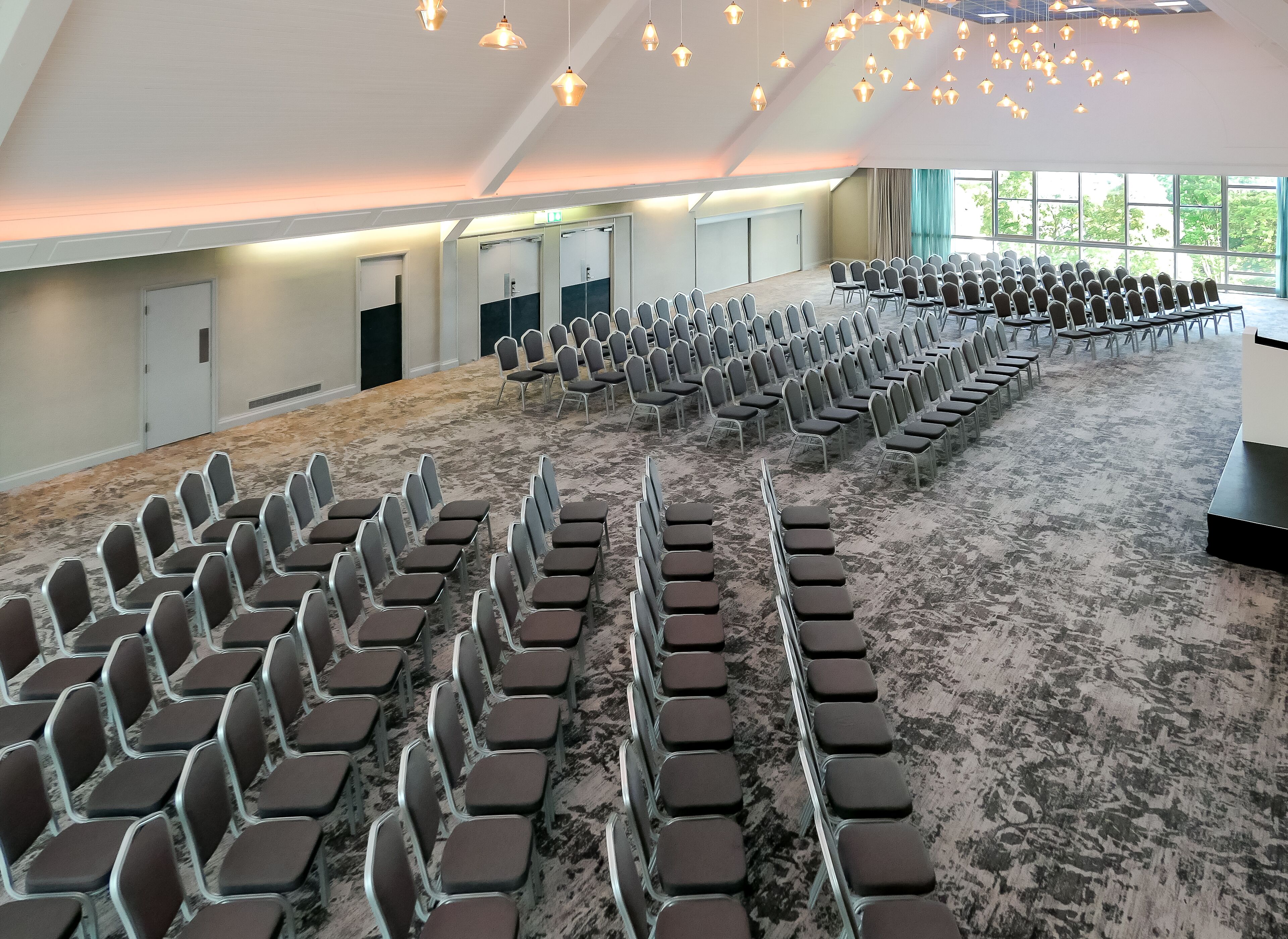 A conference room with rows of chairs, a carpeted floor, and a large window with a view of trees.