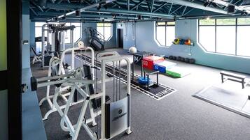A gym with weightlifting equipment, a bench, and a wall-mounted rack with weights.