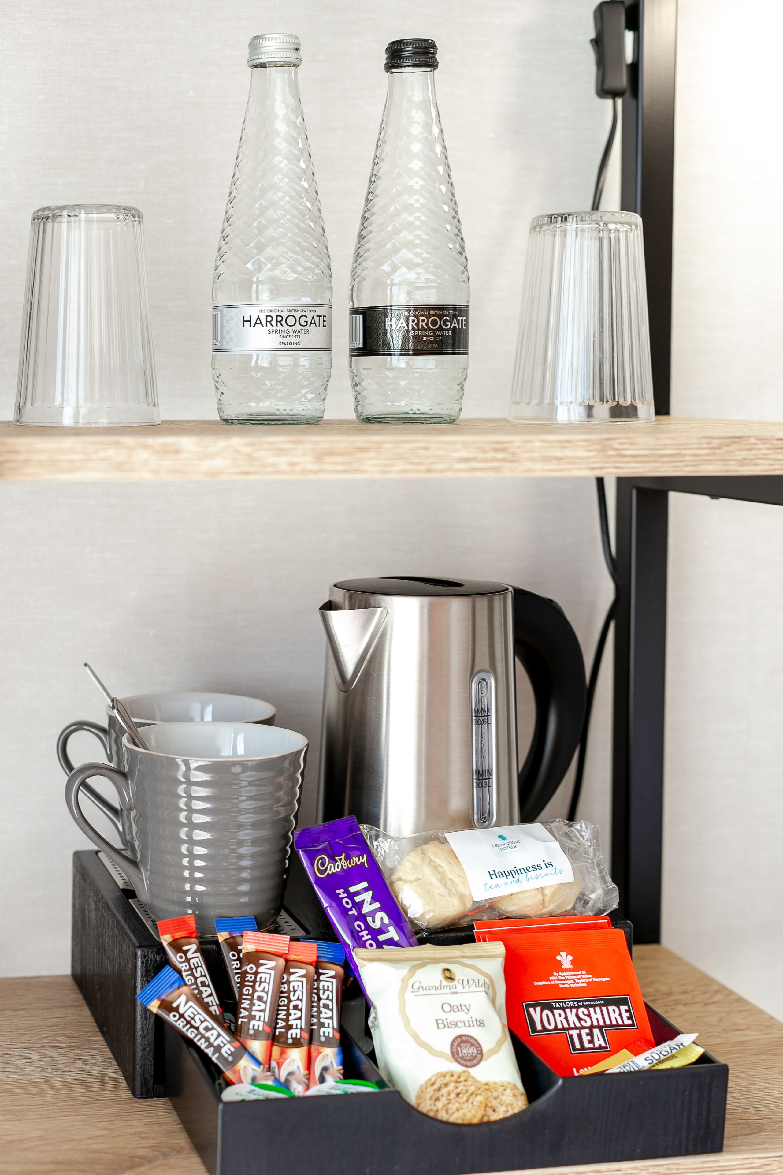 A hotel minibar with a selection of beverages, including Harrogate sparkling water, and a variety of snacks and tea.