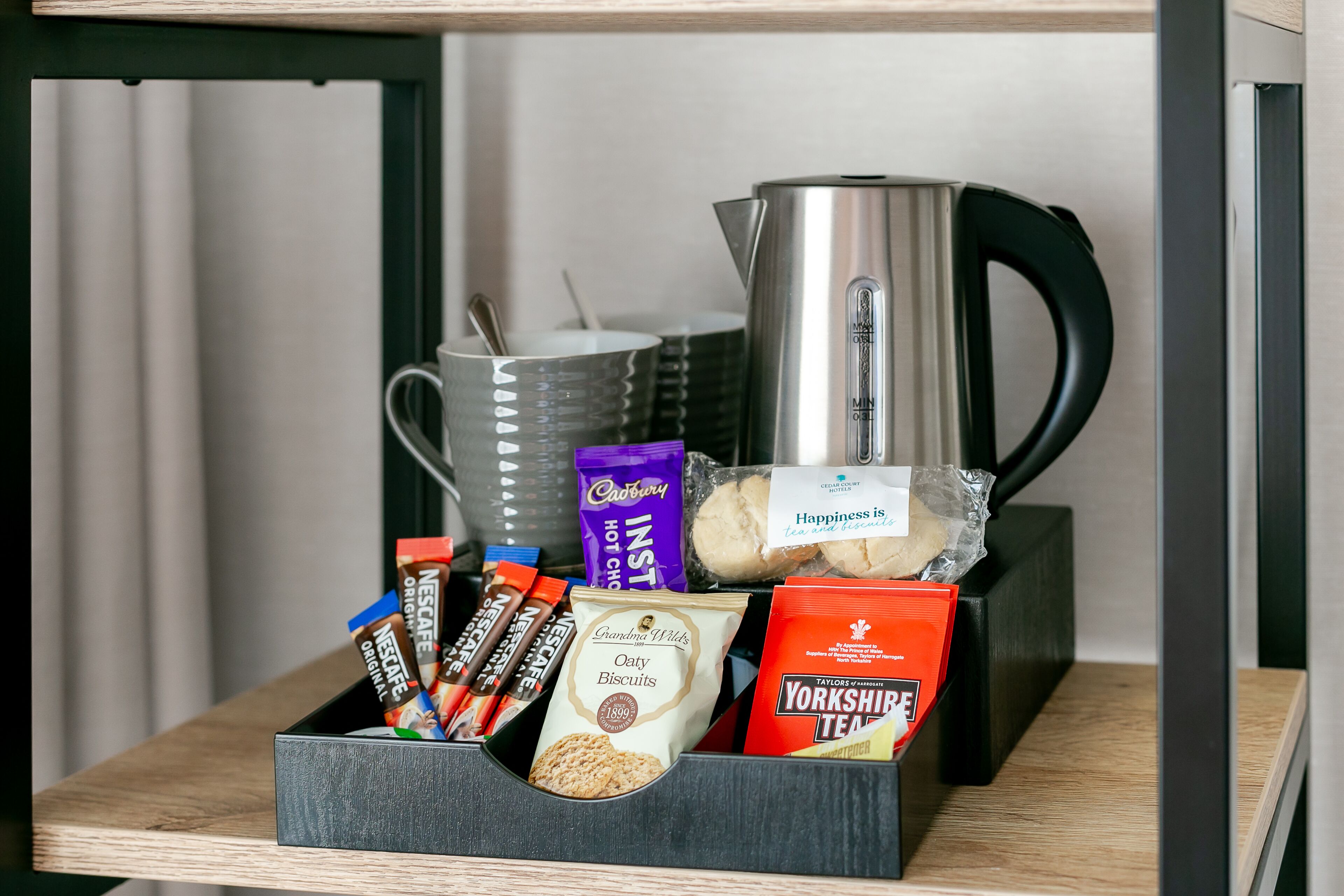 A shelf with a variety of food items including biscuits, chocolate bars, and a Yorkshire Tea packet.