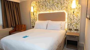 A hotel room with a large bed, two bedside tables, a chair, and a patterned headboard.