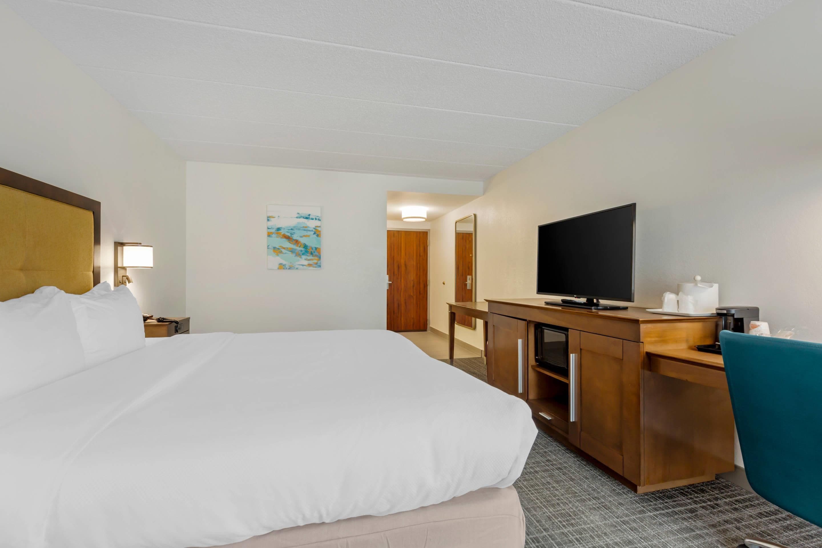 Ein Hotelzimmer mit einem großen Bett, einem Schreibtisch mit Fernseher, einem Spiegel und einer kleinen Kommode.
