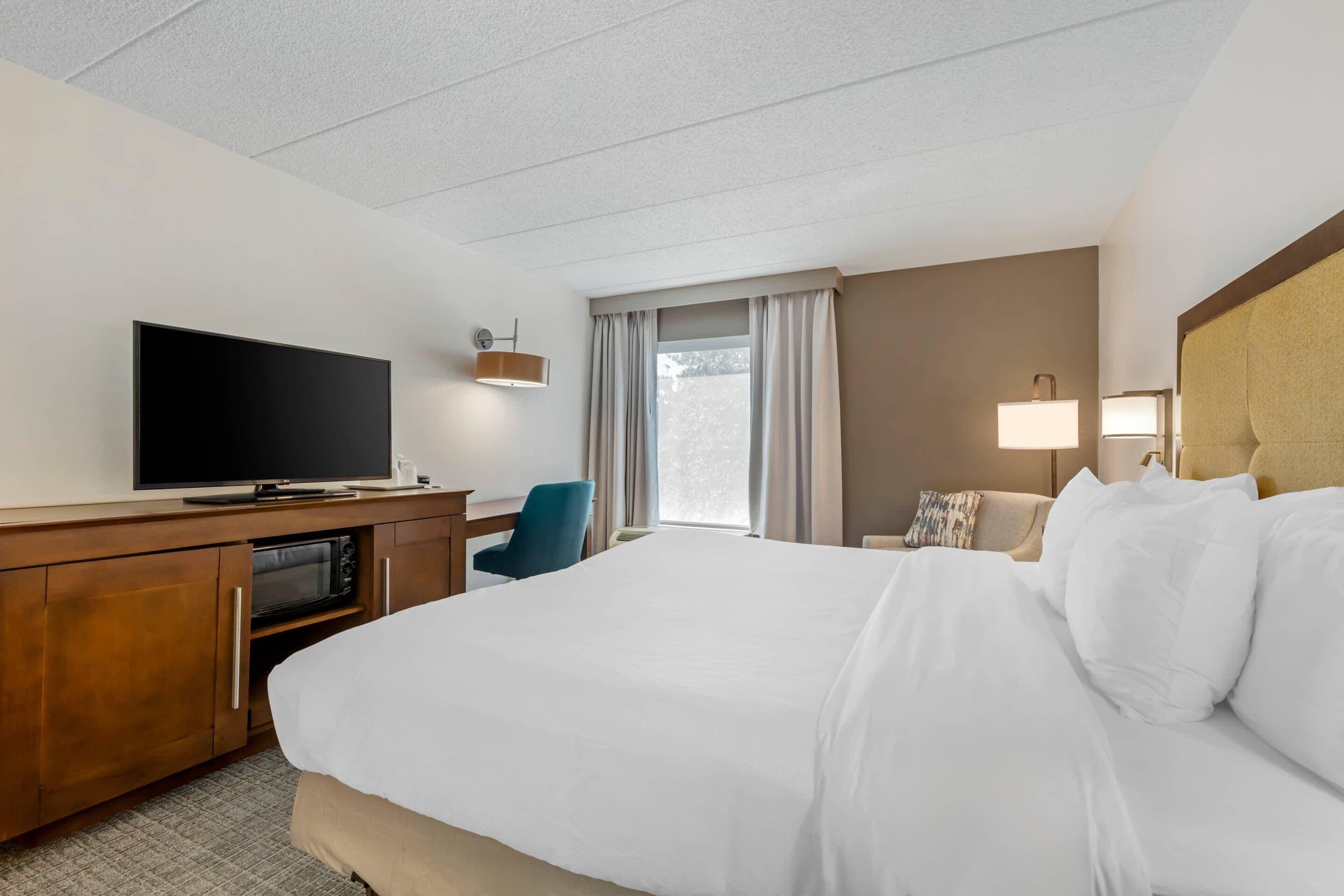 Habitación de hotel con cama, escritorio, televisor de pantalla plana, microondas, silla y ventana con cortinas.
