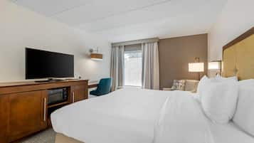 Habitación de hotel con cama, escritorio, televisor de pantalla plana, microondas, silla y ventana con cortinas.