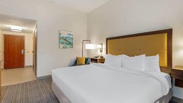 Habitación de hotel con una cama grande, una puerta de madera, una mesita de noche con lámpara y un cuadro en la pared.