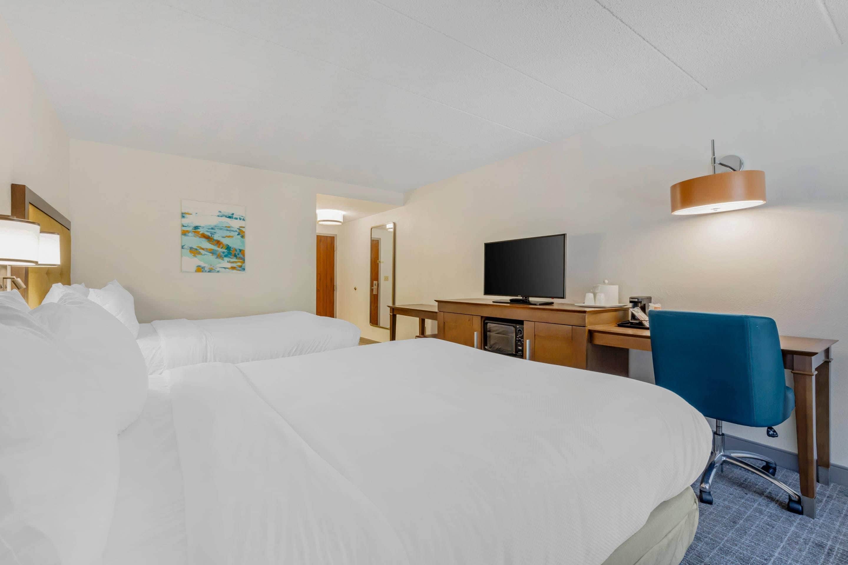 A hotel room with a bed, desk, television, and a blue chair.
