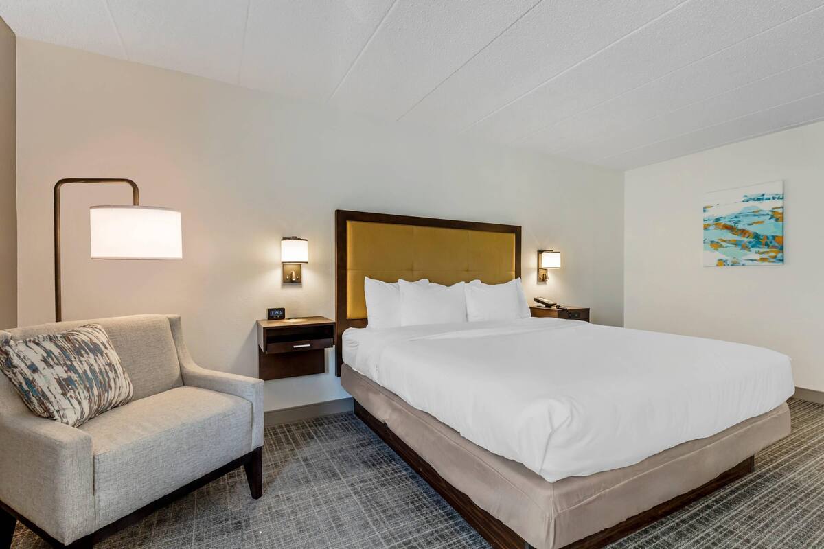 A hotel room with a large bed, a chair, bedside tables, and wall-mounted lamps.