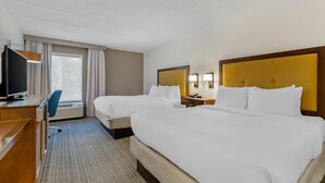 Habitación de hotel con dos camas, un escritorio, una silla, un televisor y una ventana con cortinas.