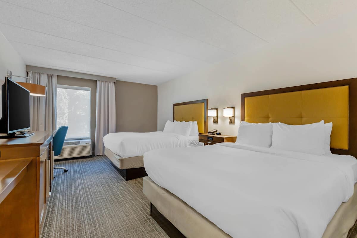A hotel room with two beds, a desk, a chair, a TV, and a window with curtains.