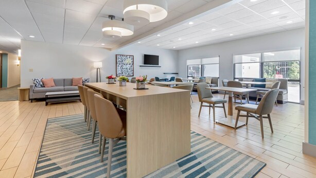 Una habitación amplia con una isla central, asientos, un sofá y un televisor montado en la pared.