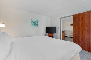 A hotel room with a bed, a TV, a wooden door, and a painting on the wall.