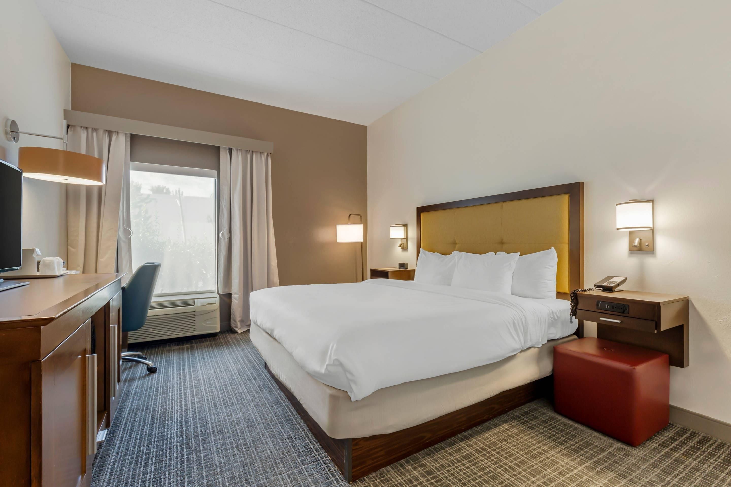 A hotel room with a bed, desk, chair, and a window with curtains.