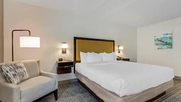 Una habitación de hotel con una cama grande, una silla, mesitas de noche y lámparas de pared.