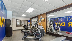 A gym with cardio machines, a mirrored wall, and a blue wall with text.