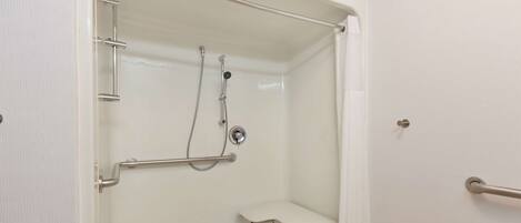 Un box de ducha blanco accesible, con barra de apoyo, asiento y ducha de mano.