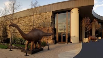 Um edifício com fachada de pedra, grande entrada de vidro e uma estátua de dinossauro à frente.