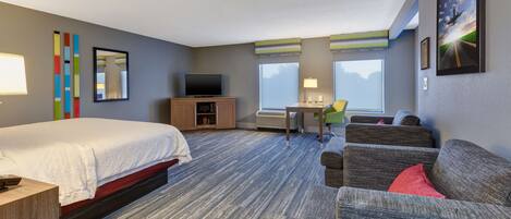 A hotel room with a bed, a desk, a television, a sofa, and a large window.