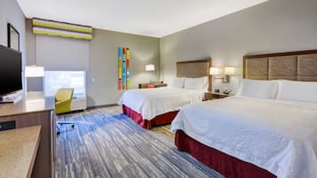 Habitación de hotel con dos camas, un escritorio, una silla y un ventanal grande.