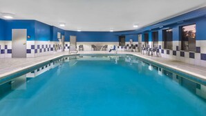 Uma piscina com paredes azulejadas em azul e branco, chão de azulejos e várias cadeiras ao redor.