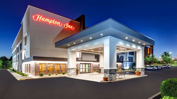 Um hotel Hampton Inn moderno com um letreiro de neon chamativo, entrada coberta e área de estacionamento.