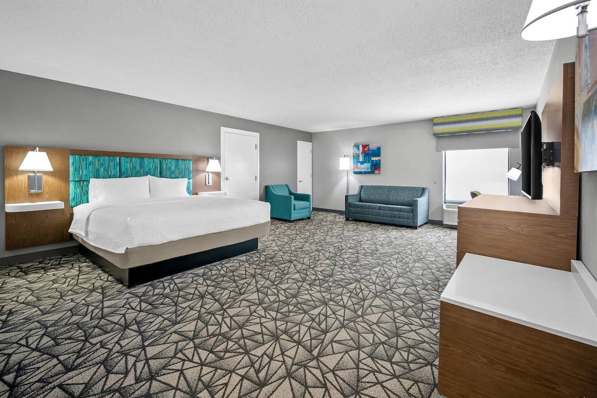 A hotel room with a large bed, a desk, a chair, a sofa, and a painting on the wall.
