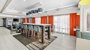A modern dining area with a rectangular table, six chairs, and a patterned rug. - Hampton Inn Bloomington West (Bloomington)