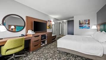 Ein Hotelzimmer mit einem Bett, einem Schreibtisch, einem Flachbildfernseher, einem Stuhl, einem Spiegel und Kunstwerken an den Wänden.