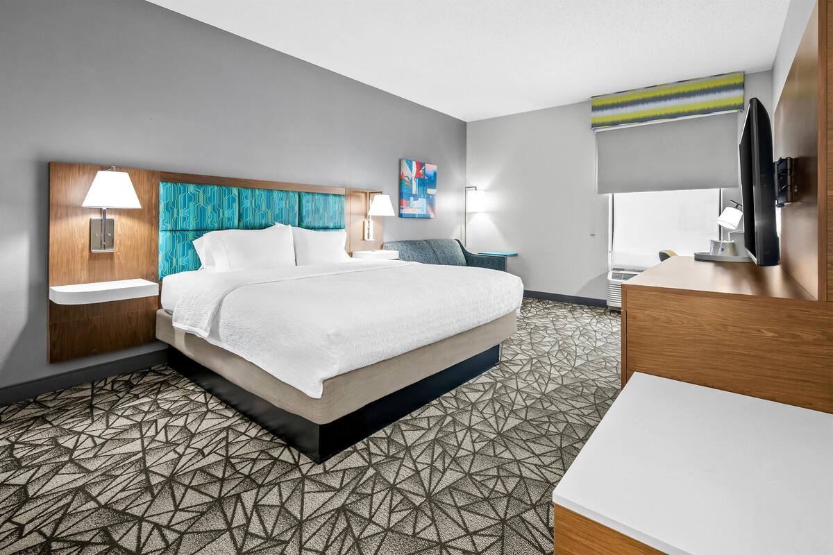 A hotel room with a large bed, a desk, a TV, and a bathroom.