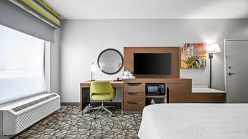 A hotel room with a bed, a desk with a computer, a microwave, a TV, and a window with a view.