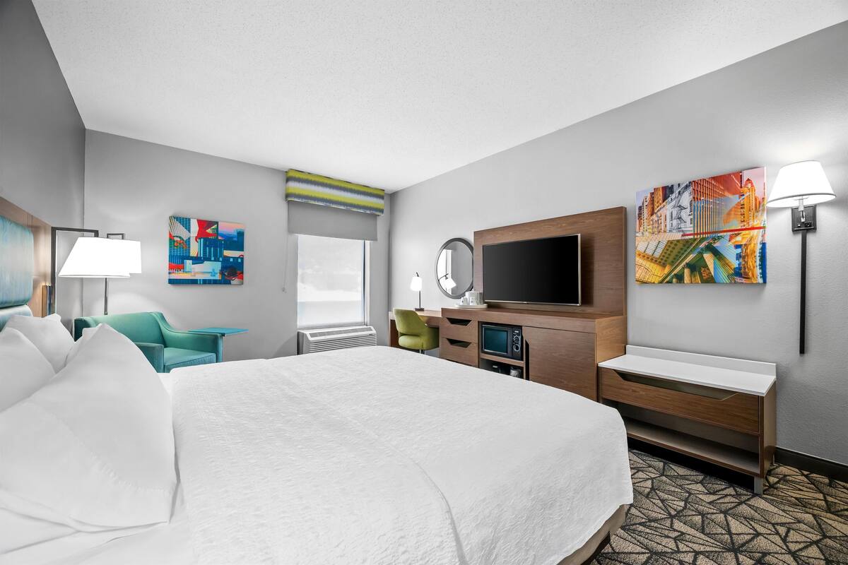 A hotel room with a large bed, a desk, a television, and artwork on the walls.