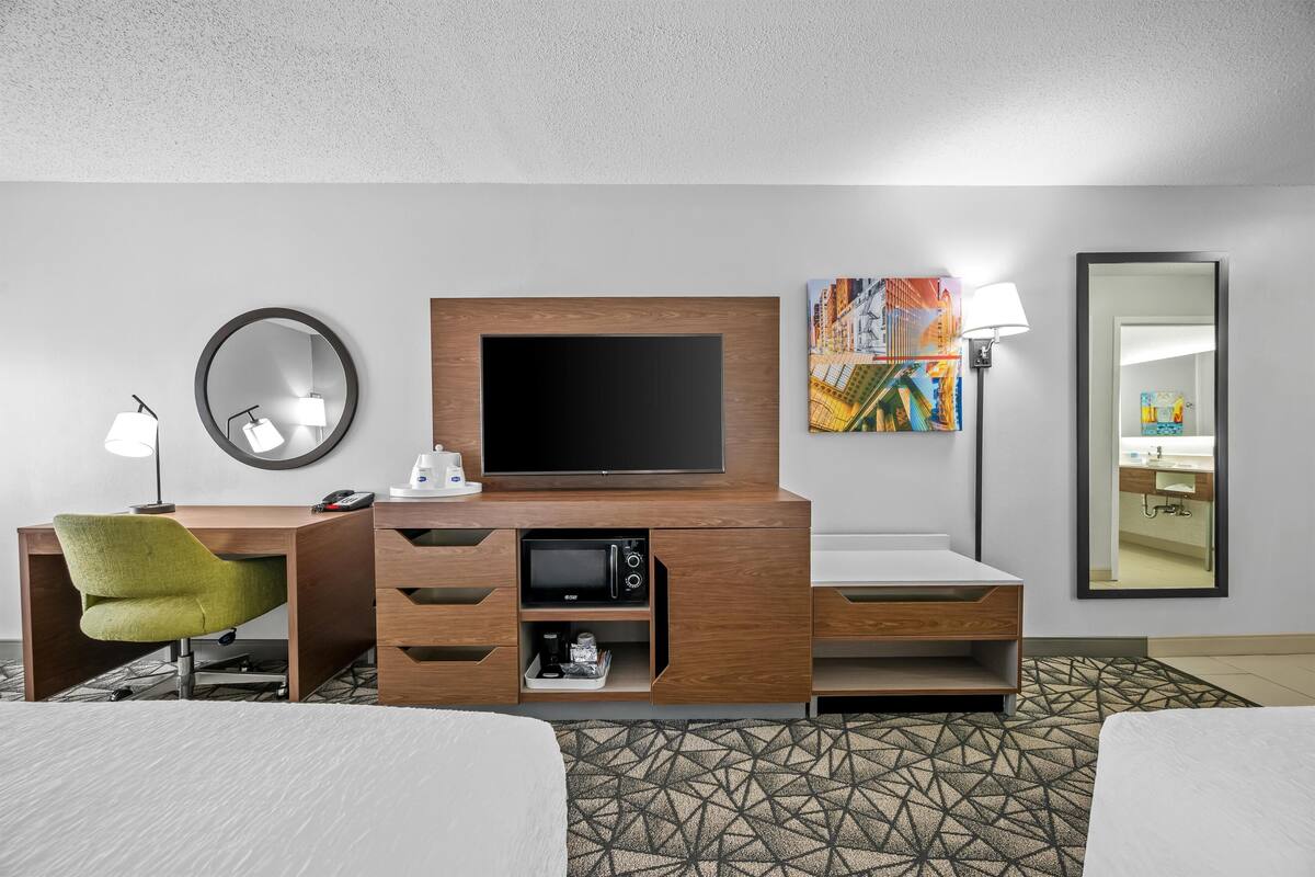 A hotel room with a wooden desk, a television, a green chair, a patterned rug, and a bed.