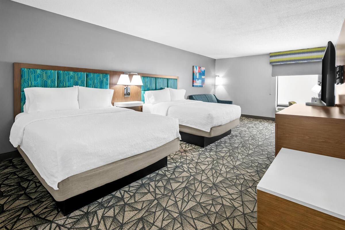 A hotel room with two beds, a desk, a chair, and a television.