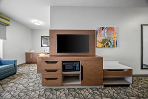 Una habitación de hotel moderna con televisión de pantalla plana, microondas y zona de estar con alfombra estampada.