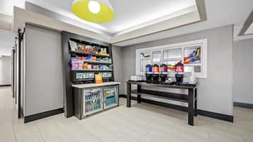 Et moderne værelse med kaffestation, hylder med snacks og et køleskab.