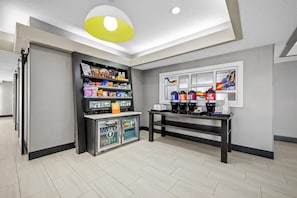A modern room with a coffee station, snack shelves, and a refrigerator.