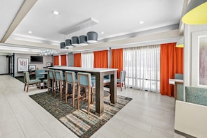 A modern hotel room with a dining area, a flat-screen TV, and a large window with orange curtains. - Hampton Inn Bloomington West (Bloomington)